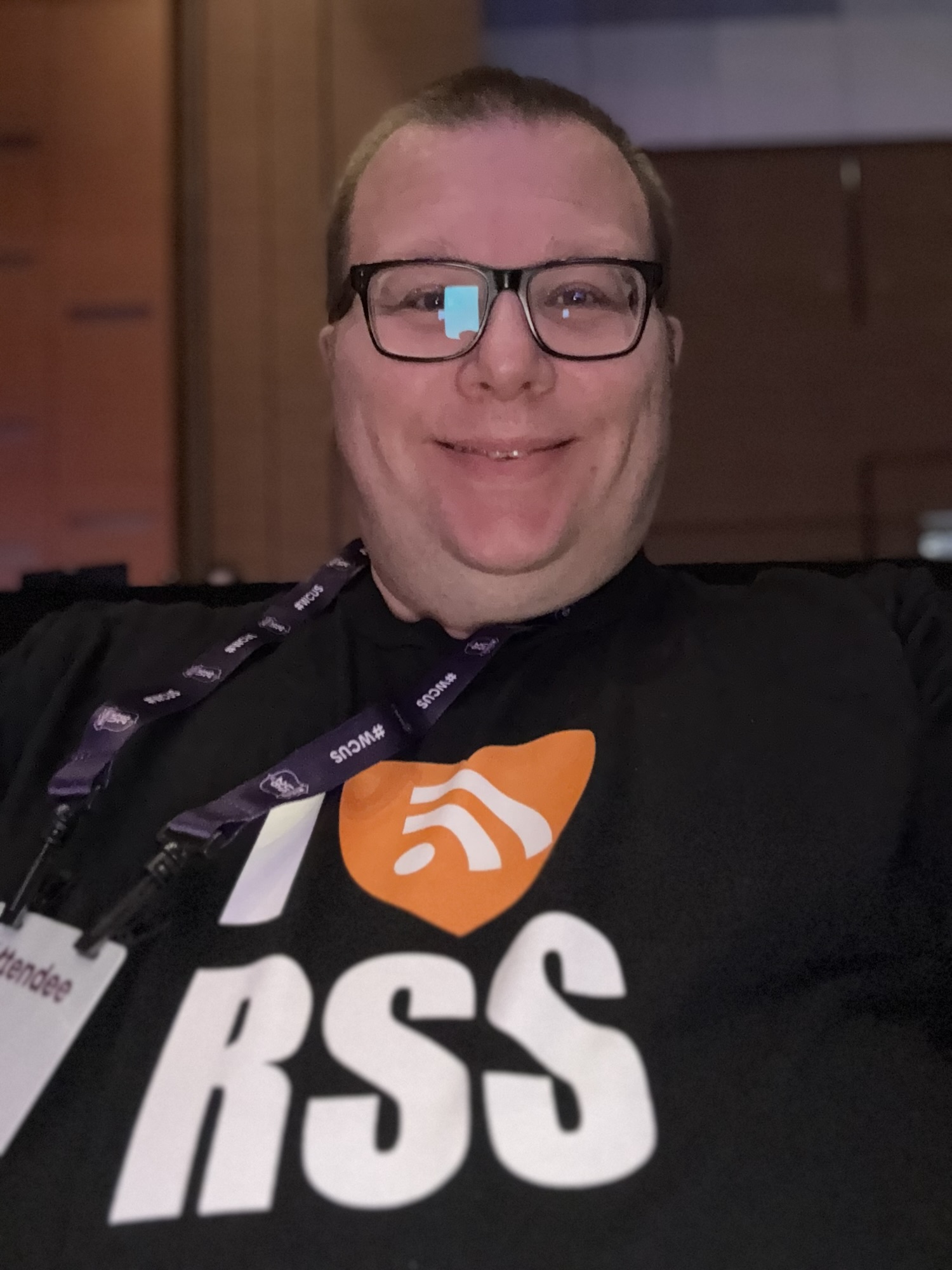 Andrew smiling in a selfie at WordCamp US, wearing a black I ♥ RSS t-shirt and a #WCUS lanyard.